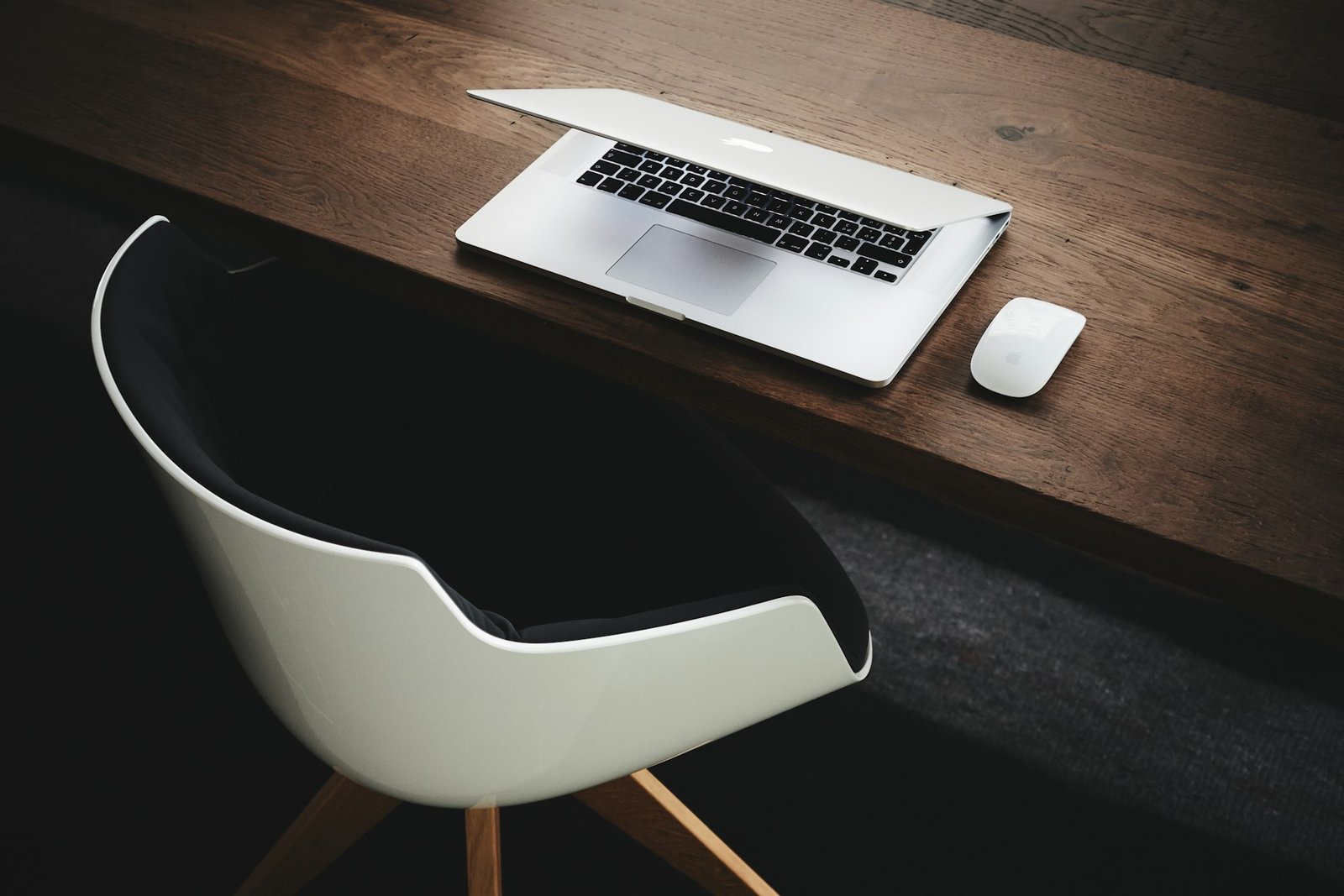 A desk with a laptop, a mouse and a white chair