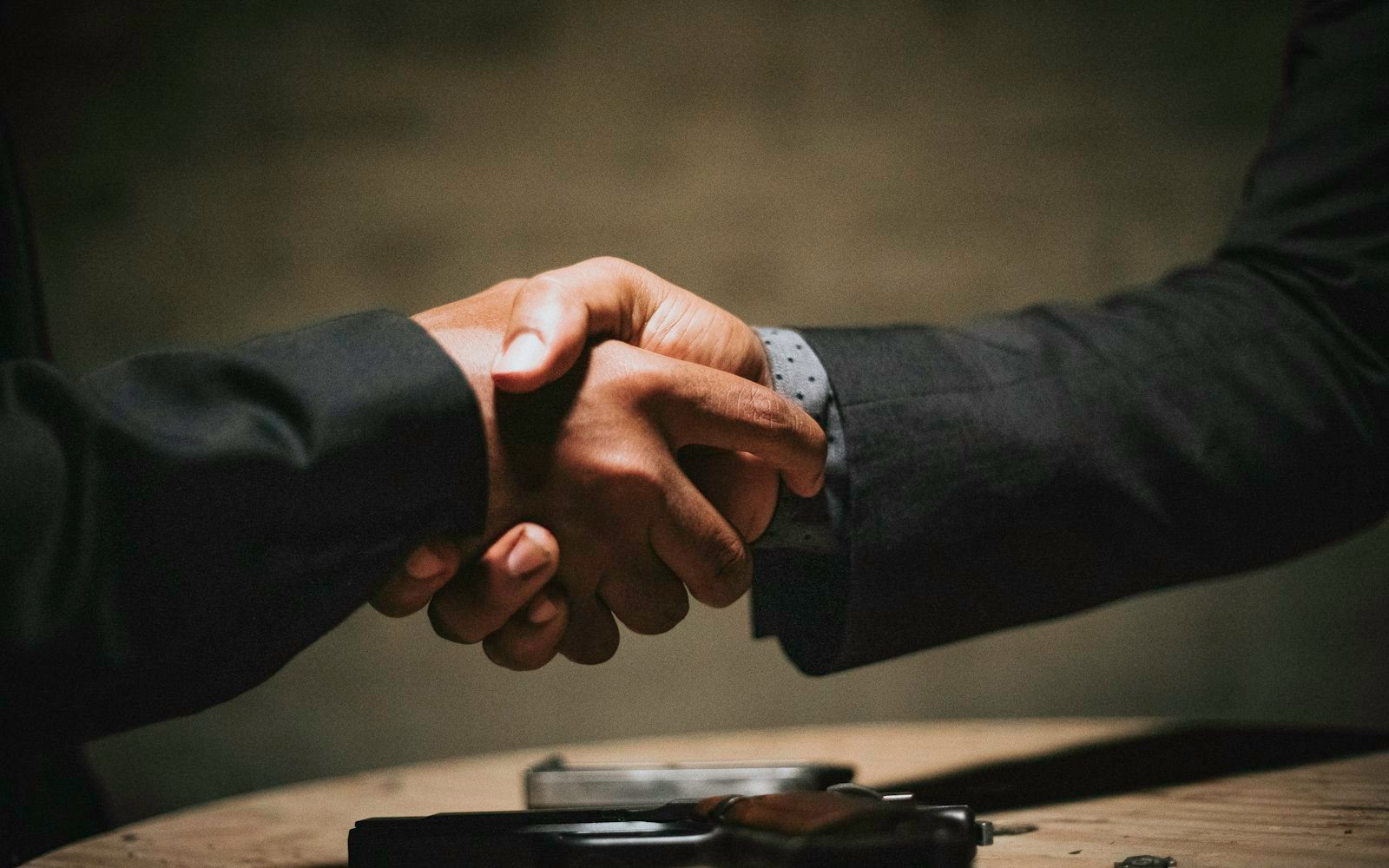 Two people shaking hands across a wooden table