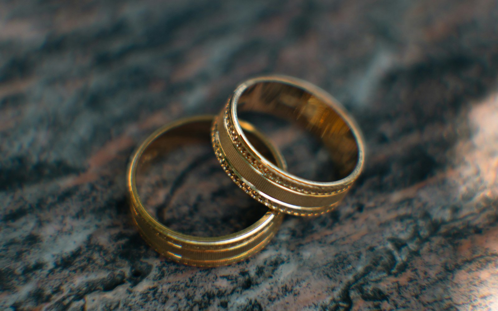 Two gold wedding rings on a dark surface