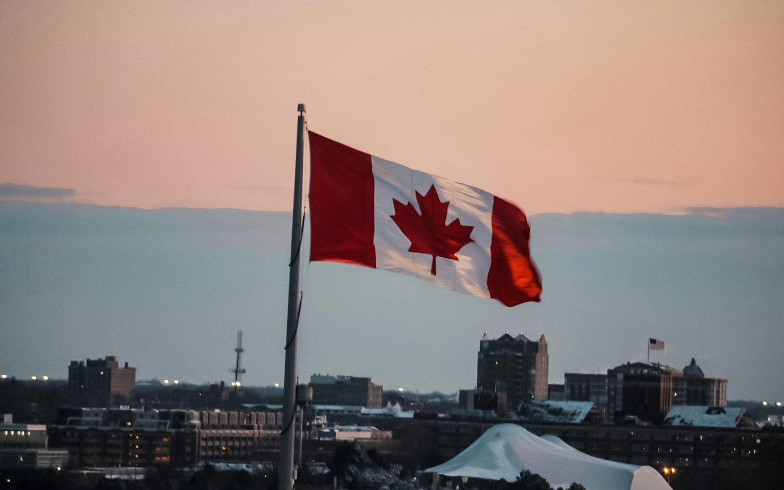 A Canadian flag flying above a city at dusk