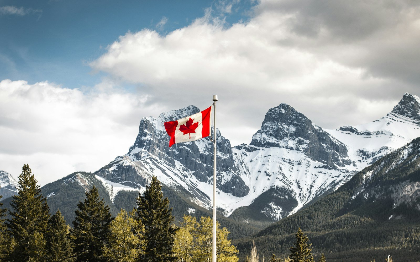 A Canadian flag flying in front of snow-covered mountains